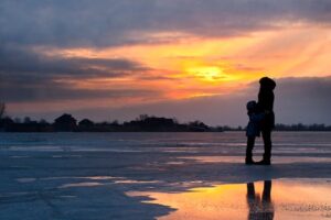 A serene sunset scene of a family silhouette on a frozen lake in Kherson, Ukraine.